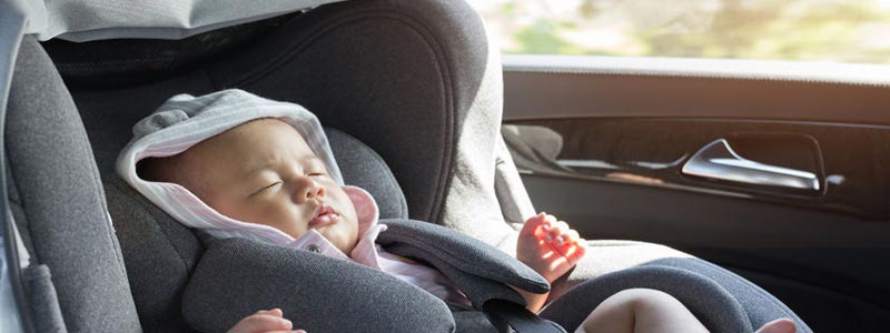 A newborn baby sitting in a car seat in a hot car.